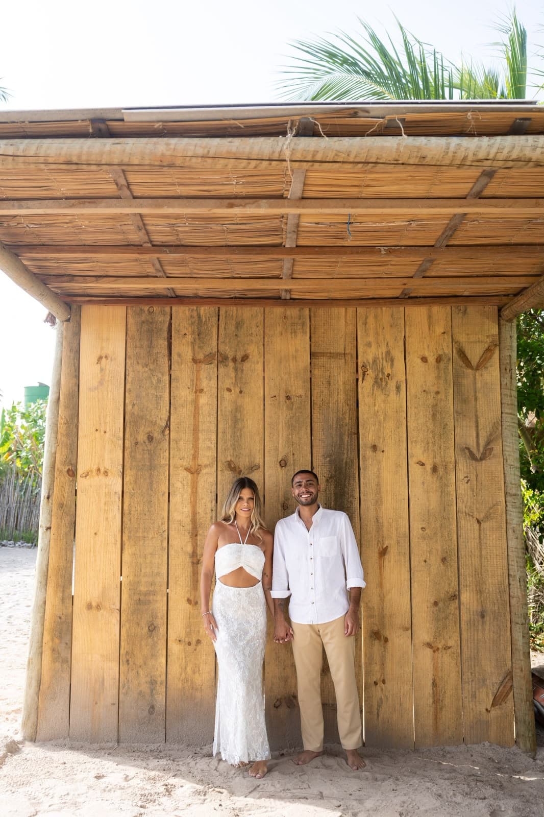 Camila e Victor de mãos dadas diante de uma parede de madeira rústica