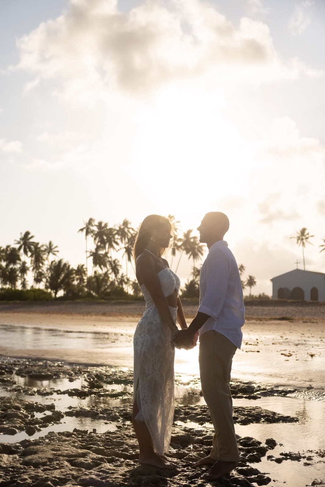 Casal de mãos dadas em silhueta ao pôr do sol, sobre os recifes