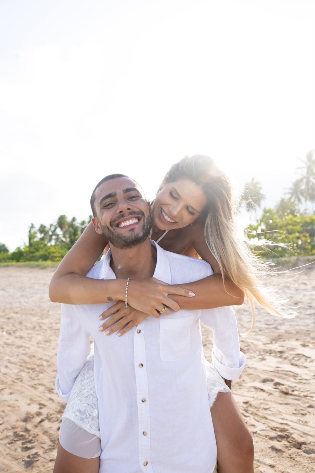 Camila nas costas de Victor, os dois sorrindo na praia