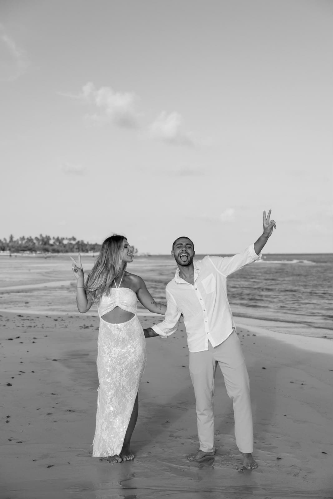 Casal brincando e fazendo sinal de paz na beira do mar, em preto e branco