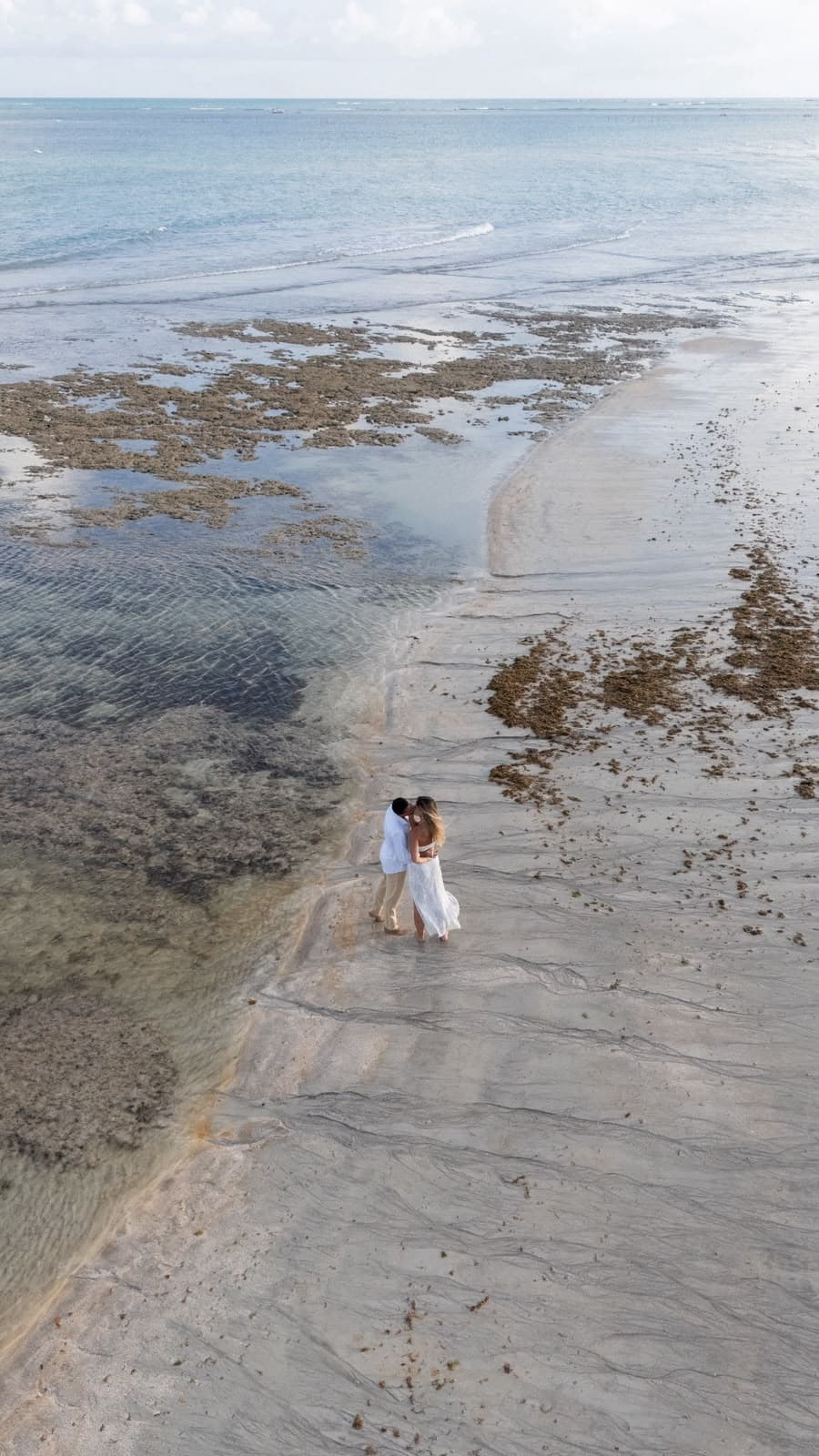 Vista aérea do casal se beijando na faixa de areia entre os recifes